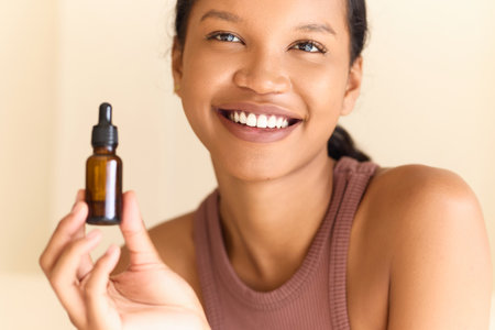 Smiling Woman Holding Skincare Serum Bottle in Natural Light Settingの写真素材