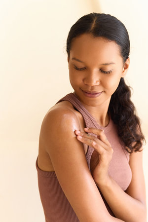 Young Woman Gently Applying Moisturizer to Her Shoulder for Skincare Routineの写真素材
