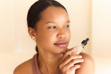 Thoughtful Woman Holding Skincare Serum Bottle Against Neutral Backgroundの写真素材