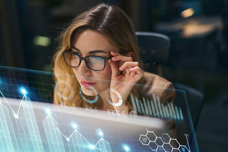 Focused Businesswoman Analyzing Digital Data on a Transparent Interactive Screen at Nightの写真素材