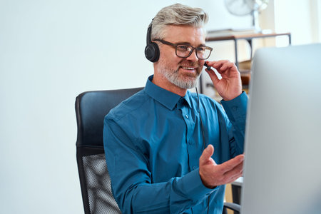 Senior Man Communicating Online Using Headset in Home Office Workspace