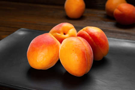 Apricots on a dark background. Four fresh juicy ruddy apricots are stacked in a dark clay plate on a wooden table. Close-up healthy organic food.の写真素材