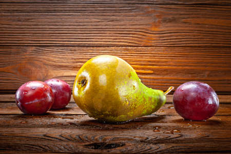 One wet brown pear and ripe plums with drops of water on a dark wooden background. Organic foods, healthy nutrition.の写真素材