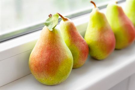 Pears on a white windowsill. Close-up juicy ripe pears are stacked in a row near the window. Fruit...