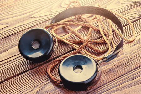 Old headphones for the radio. Close-up of vintage headphones with fabric wire on wooden background. The concept of ancient radio engineering. Selective soft focus.の写真素材