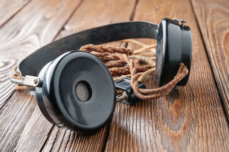 Old headphones. Vintage headphones with a cloth wire on a wooden background. The concept of ancient radio engineering. Selective soft focus.の写真素材