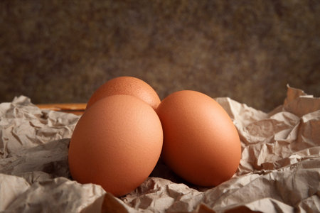 Chicken eggs. Raw brown chicken eggs on crumpled wrapping paper on a dark background. High calorie...