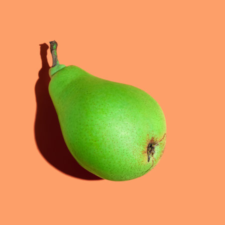 green pear. Ripe juicy pear on an orange background close-up. Ripe fruit. sharp shadowの写真素材