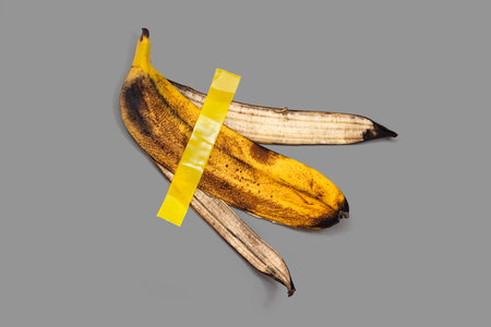 Banana peel is glued together with tape. Gray background. Conceptual satirical photoの写真素材