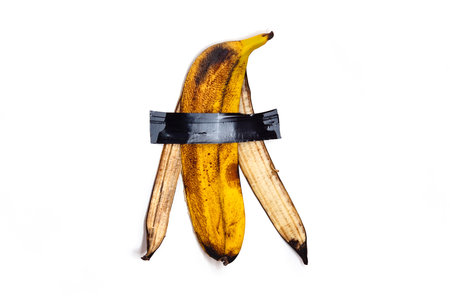 Peel of a yellow ripe banana is glued with tape. Isolated on white background. Conceptual photoの写真素材