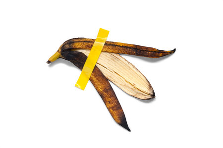 Peel of a yellow ripe banana is glued with yellow tape. Isolated on white background. Conceptual photoの写真素材