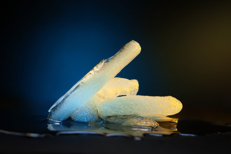 Ice melting. Melting ice chunks on dark. Colored blue yellow backlight. Selective soft focus