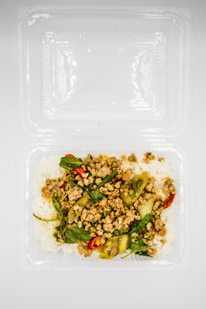 Rice topped with stir-fried pork and basil in a box placed on a white ground.の写真素材