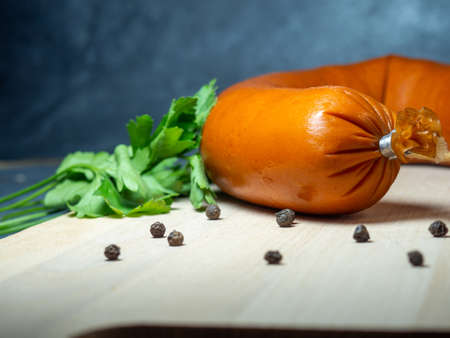 The sausage lies on a kitchen board with pepper and and parsley leavesの写真素材