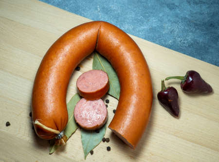 The sliced ââchicken sausage lies on a kitchen board with black peppercorns, chilli peppers and bay leaves.の写真素材