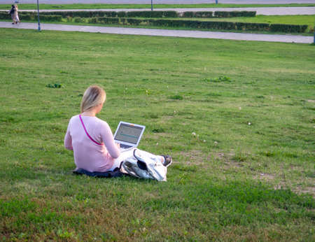 Girl working in a laptop on the lawn in the cityの写真素材