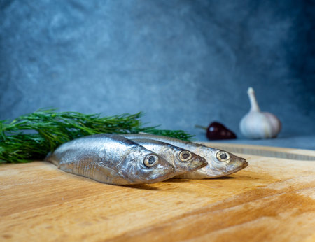 sprat on a cutting board. Whole fish, pepper, dill and garlic on the table. Snack. Cookingの写真素材