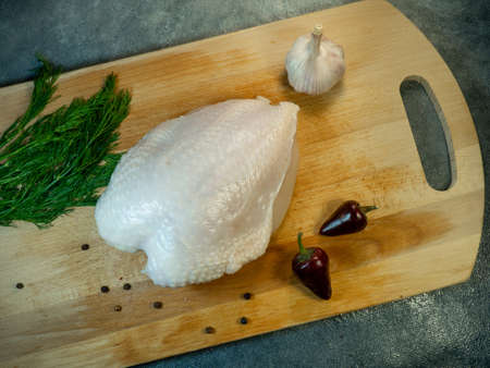 Chicken breast   on a cutting board. Still life on a black background. Multi-colored peppercorns, dill, hot pepper and garlic around a piece of meat.  view from aboveの写真素材