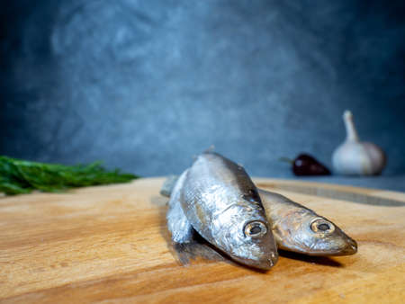 sprat on a cutting board. Whole fish, pepper, dill and garlic on the table. Snack. Cookingの写真素材