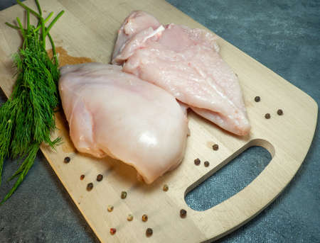 Chicken breast fillet on a cutting board on a black background. Peppercorns and dill around a piece of meat.  Cooking chickenの写真素材