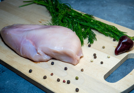Chicken breast fillet on a cutting board on a black background. Peppercorns, hot pepper and dill around a piece of meat.  Cooking chickenの写真素材