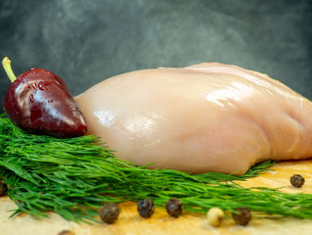 Chicken breast fillet on a cutting board on a black background. Peppercorns around a piece of meat. Dill and hot peppers. Cooking chickenの写真素材