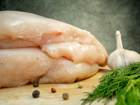 Chicken breast fillet pieces on a cutting board. Still life on a black background. Multi-colored peppercorns, garlic and dill around a piece of meat.  Cooking chicken. Raw meat.の写真素材