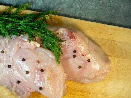 Chicken breast fillet on a cutting board on a black background. Peppercorns and dill around a piece of meat.  Cooking chickenの写真素材