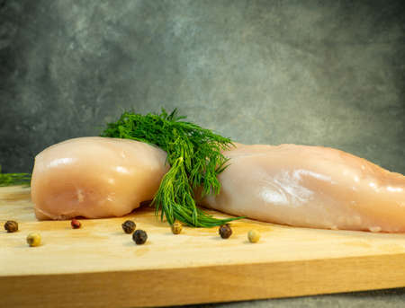 Chicken breast fillet on a cutting board. Still life on a black background. Multi-colored peppercorns around a piece of meat. Cooking chicken. Raw meat.の写真素材