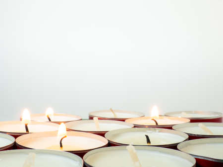 Short candles are burning against a white background. Lots of small candles. Not all candles are lit. Extinguishedの写真素材