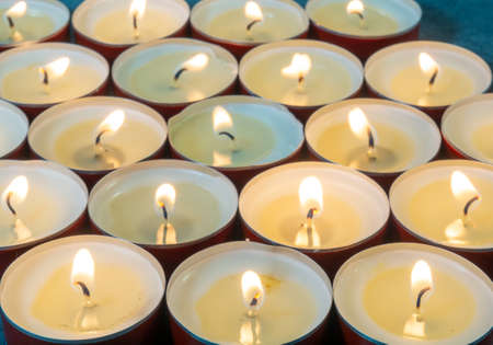 Lots of small lit candles. Dark mysterious atmosphere. Candle background. Flat round candlesの写真素材