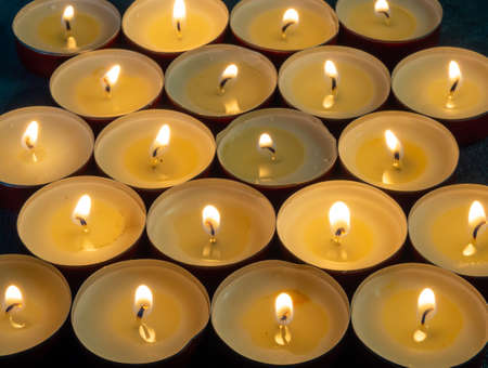 Lots of small lit candles. Dark mysterious atmosphere.Candle background.Flat round candles in red metal standsの写真素材