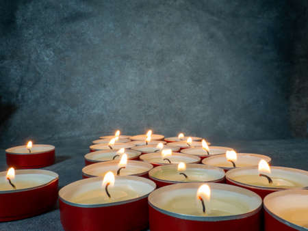 Lots of small lit candles. Dark mysterious atmosphere. Candle background. Flat round candlesの写真素材