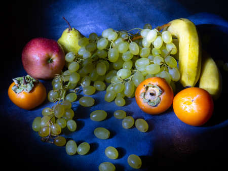 Still life of fruits. apple, persimmon, pear and grapes on a black background. Persimmon Chamomile. Apple Gala. Pear Lucas. Healthy eating. Vegetarianism. Water droplets on the fruitの写真素材