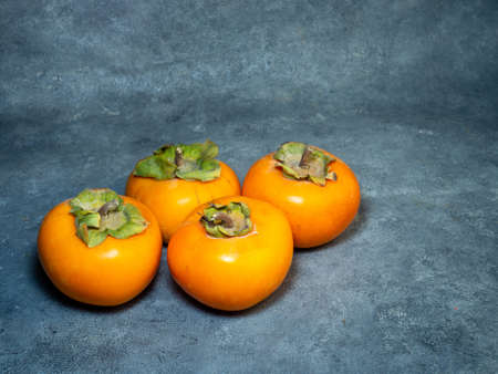 Four persimmons on a black background. Persimmon varieties Chamomile. still life. Big ripe tasty fruits on the tableの写真素材