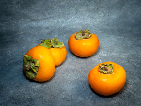 Four persimmons on a black background. Persimmon varieties Chamomile. still life. Big ripe tasty fruits on the table.の写真素材