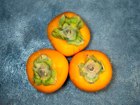 Four persimmons on a black background. Persimmon varieties Chamomile. still life. Big ripe tasty fruits on the tableの写真素材