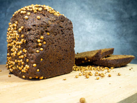 Sliced ââbrown bread sprinkled with coriander. Borodino bread. Flour product. Bread with spices on kitchen board on black backgroundの写真素材