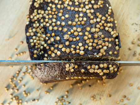 Slicing ââbrown bread sprinkled with coriander. Borodino bread. Flour product. Bread with spices on kitchen board on black backgroundの写真素材