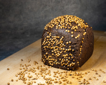 Black bread sprinkled with coriander. Borodino bread. Flour product. Bread with spices on kitchen board on black backgroundの写真素材
