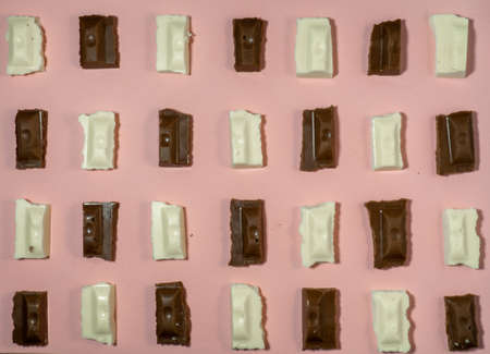 Slices of black and white chocolate on a pink background. Various chocolates on the table. Background of sweet slicesの写真素材