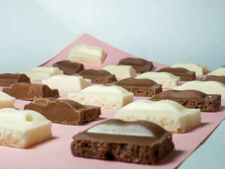 Slices of black and white chocolate on paper. Slices from a bar of chocolate. Sweet slices backgroundの写真素材