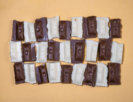 Slices of black and white chocolate on a beige background. Slices from a bar of chocolate. Sweet slices backgroundの写真素材