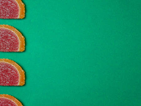 Fruit jelly in the form of orange slices on a green surface. Background from sweets. Background from marmaladeの写真素材