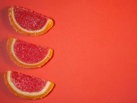 Fruit jelly in the form of orange and grapefruit slices on a red background.Sweets on the table. Background from marmaladeの写真素材