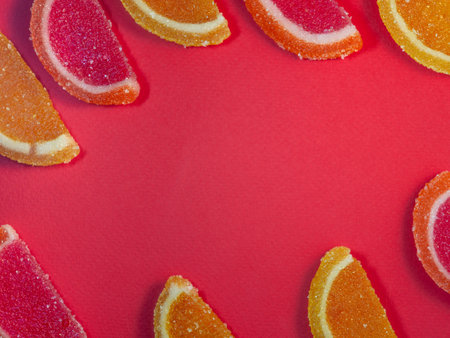 Fruit jelly in the form of orange and grapefruit slices on a red background.Sweets on the table. Background from marmaladeの写真素材