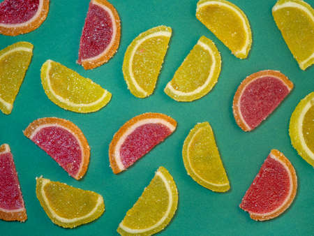 Fruit jelly in the form of orange slices on a green surface. Background from sweets. Background from marmaladeの写真素材
