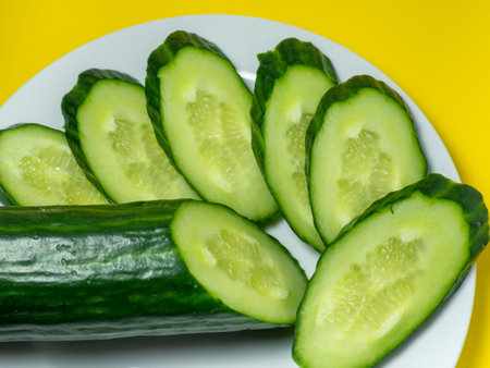 A smooth, medium-sized cucumber on a plate, sliced. Cucumber on a yellow background. Vegetable isolate.の写真素材