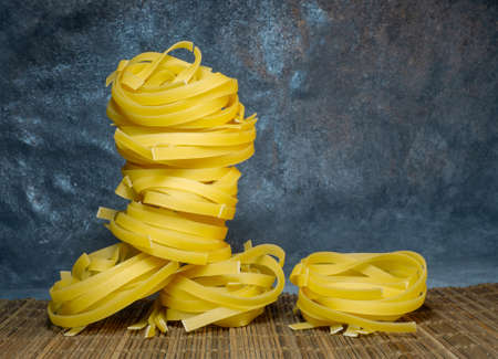 Pasta nests on a wicker background. Type of noodle. Noodle pyramid. Unprepared product. Culinary background. Cooking. Dough productsの写真素材