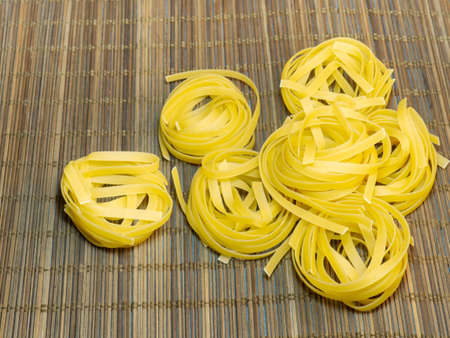 Pasta nests on a wicker background. Noodle pyramid. Unprepared product.Type of noodle. Culinary background. Cooking. Dough productsの写真素材